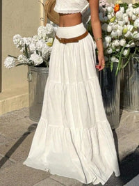 Person wearing a white dress with a brown belt, standing among potted flowers.