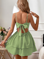 Green dress with open back worn by a person, with flowers and a chair in the background.