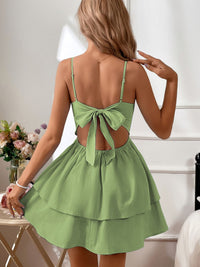 Green dress with open back worn by a person, with flowers and a chair in the background.