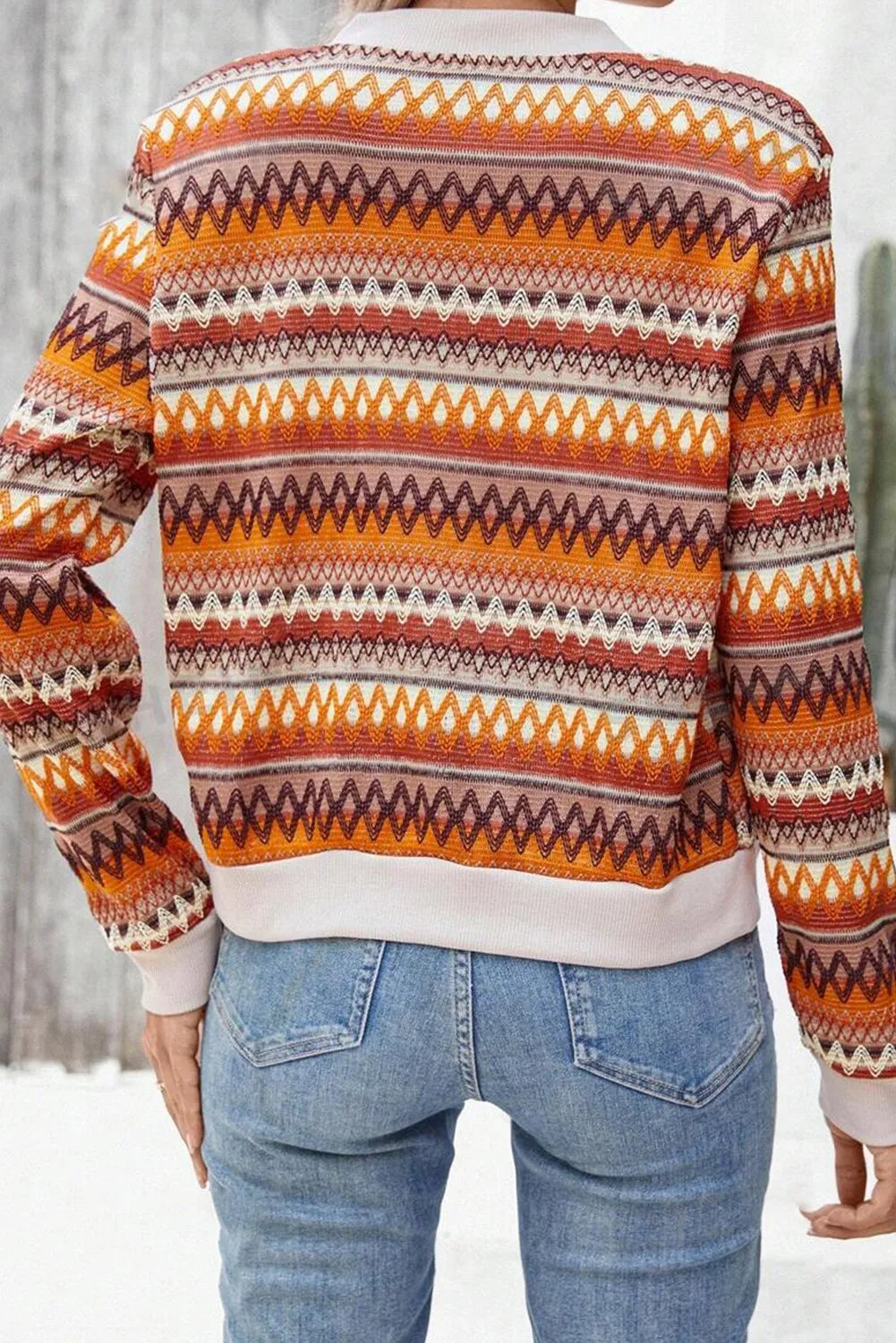 Person wearing a patterned sweater with orange, brown, and white colors in a snowy landscape.