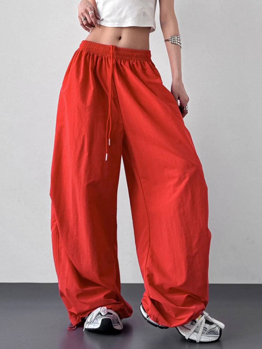 Person wearing red wide-leg pants with a white top on a gray background