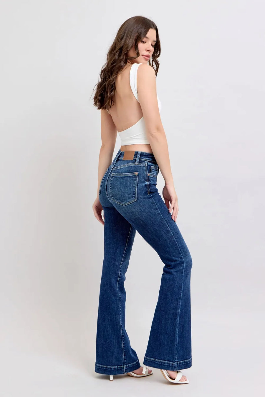 Woman wearing blue flared jeans and a white top on a light gray background
