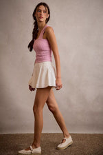 Woman wearing a pink top and white skirt against a plain background