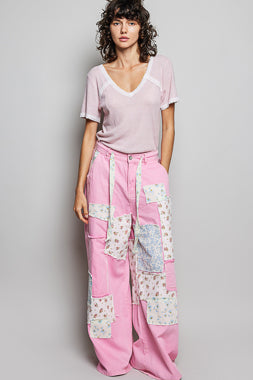 Woman wearing a pink top and patchwork pants on a gray background