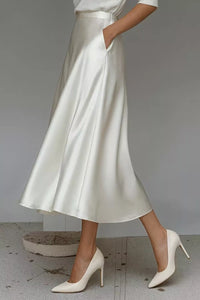 Person wearing a white satin skirt and high heels on a plain background