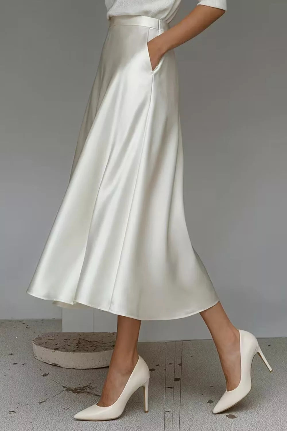 Person wearing a white satin skirt and high heels on a plain background