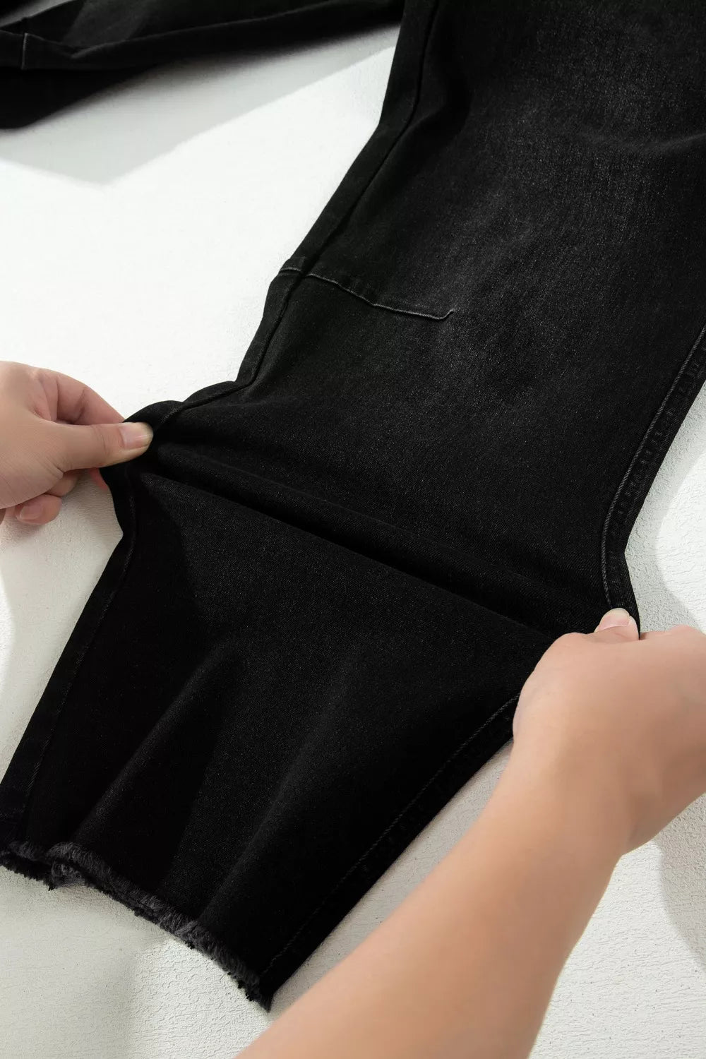 Person adjusting a black garment on a white surface