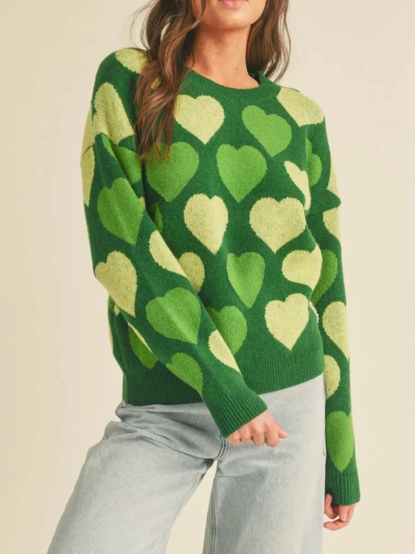 Green sweater with heart pattern worn by a person on a beige background