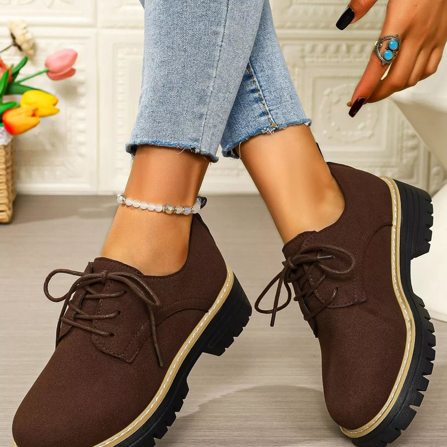 Brown shoes worn with light blue jeans on a neutral background