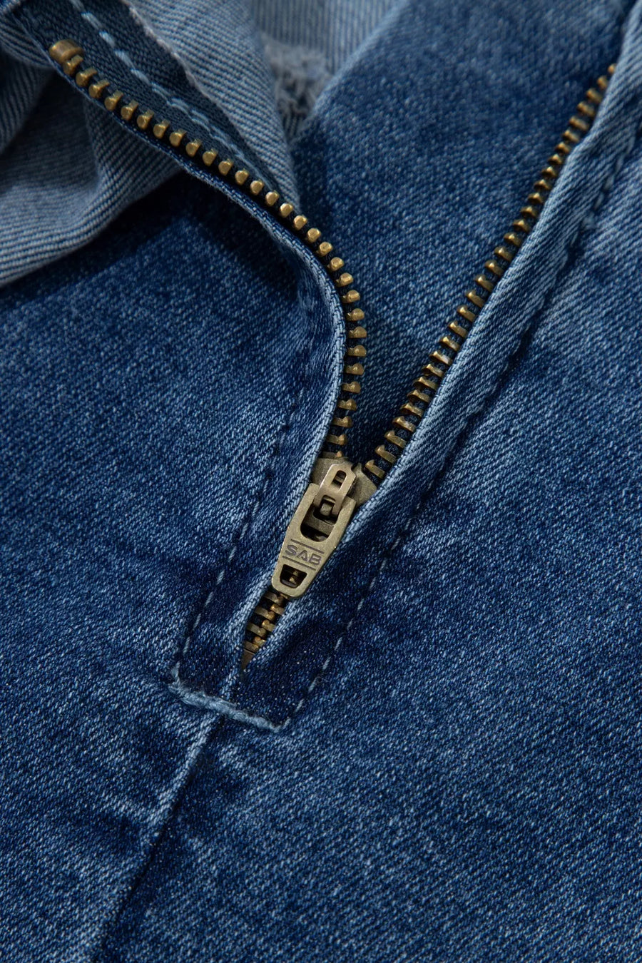 Close-up of a blue denim jacket with a gold zipper