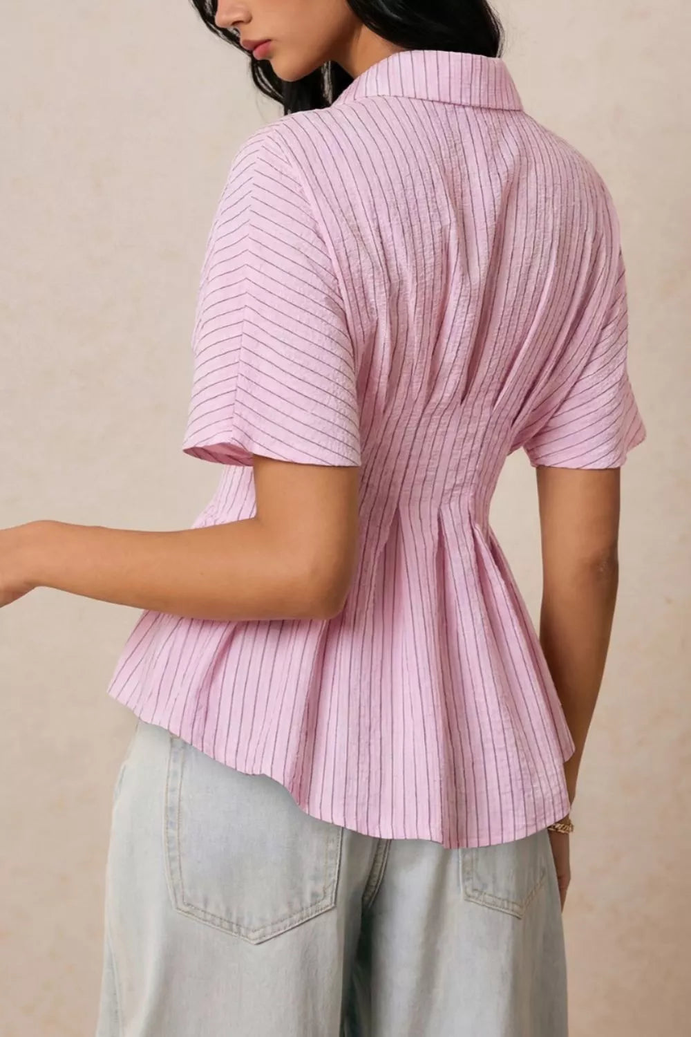 Person wearing a pink ribbed blouse with short sleeves against a beige background