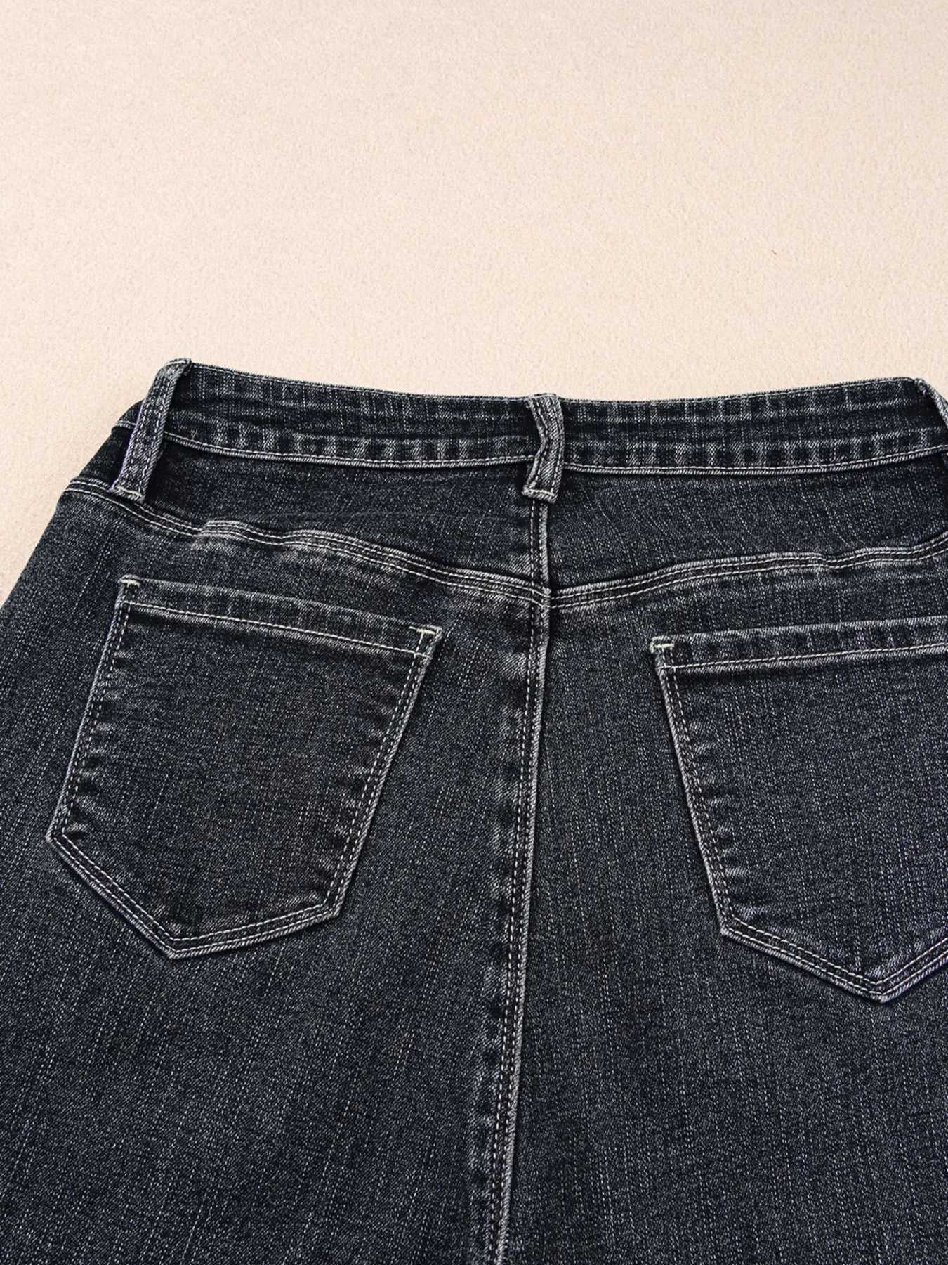 Close-up of a pair of dark blue jeans with a beige background