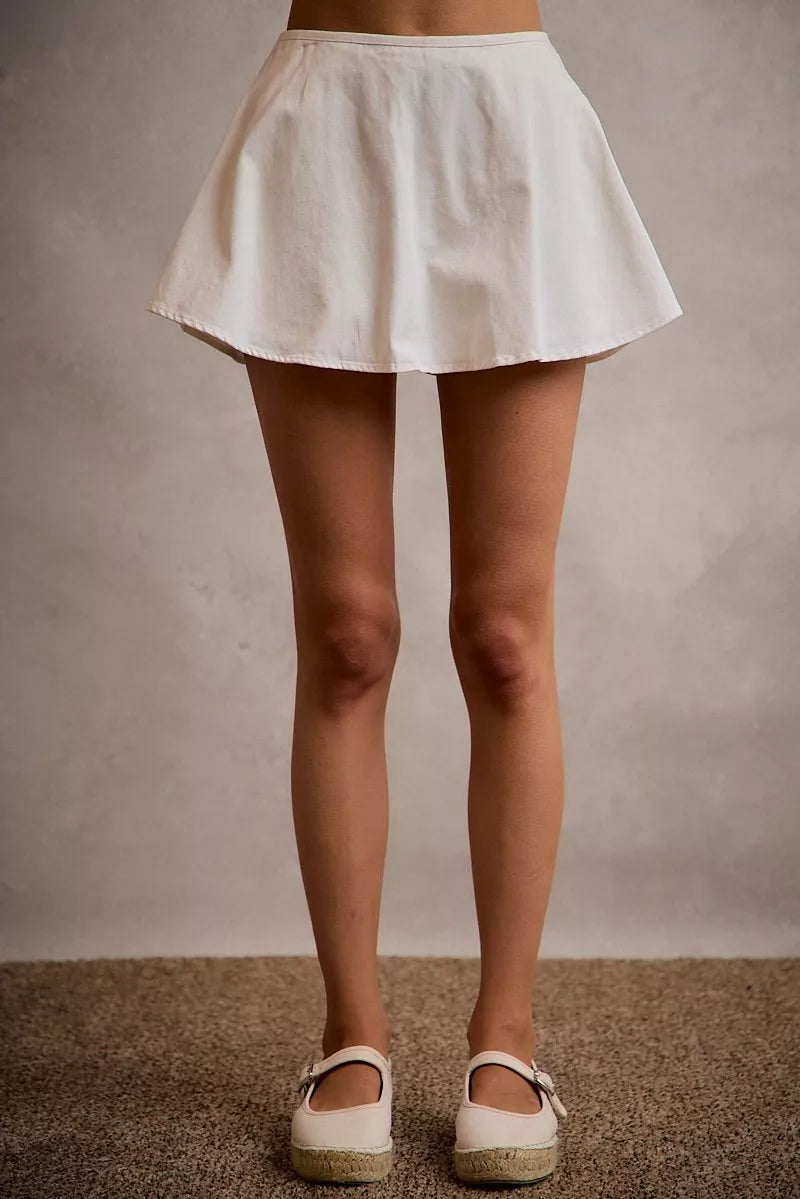 Person wearing a white skirt and white shoes on a neutral background