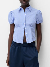 Person wearing a blue striped shirt with puffed sleeves and navy pants against a white background