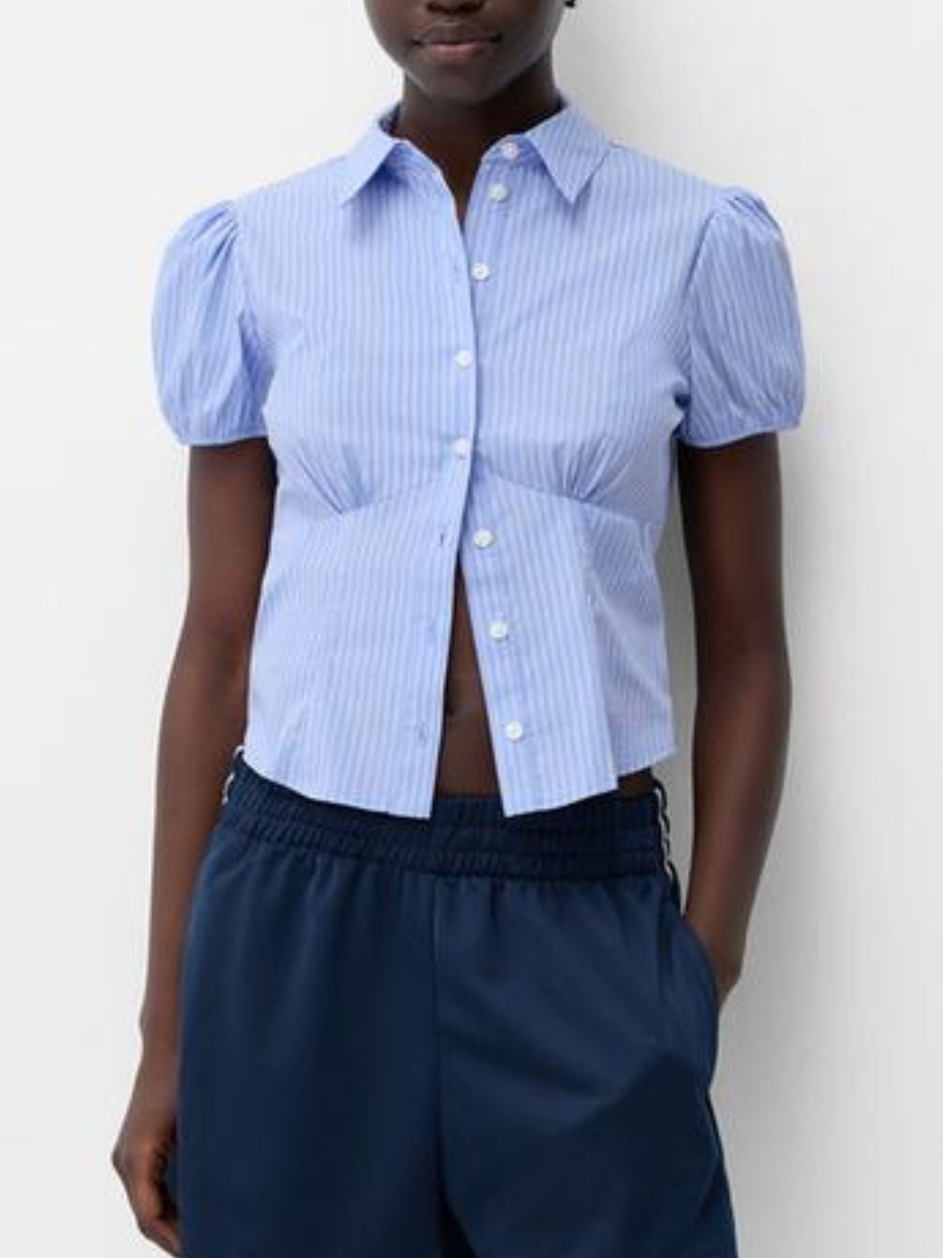 Person wearing a blue striped shirt with puffed sleeves and navy pants against a white background