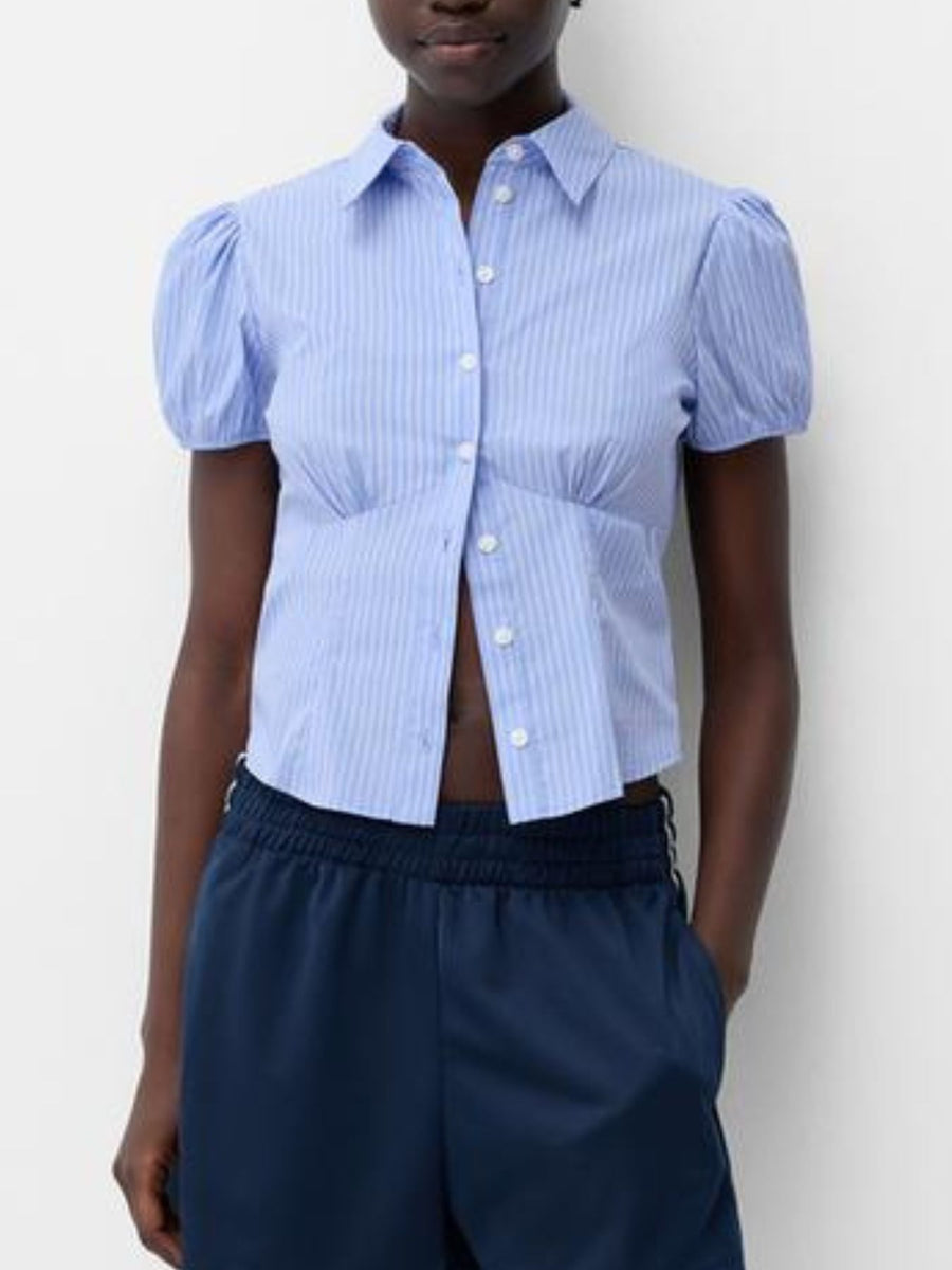 Person wearing a blue striped shirt with puffed sleeves and navy pants against a white background