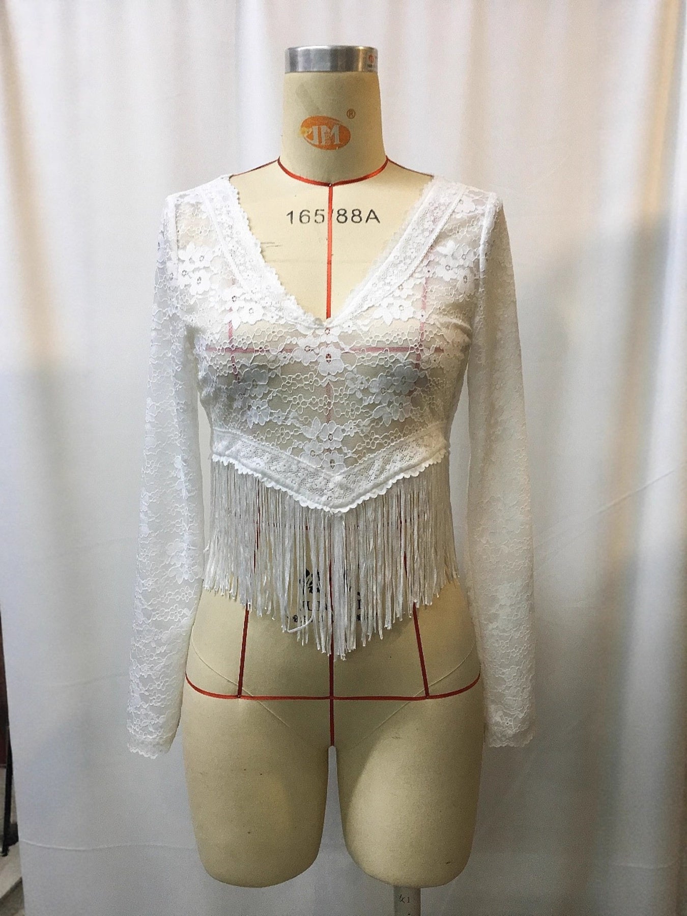 Mannequin wearing a white lace top with fringe details against a plain background