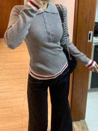 Person wearing a gray sweater with red and white stripes and dark pants indoors.