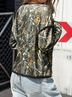 Person wearing a camouflage jacket with a red and white sign in the background