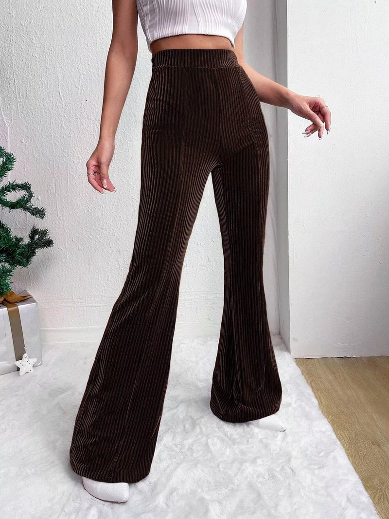 Person wearing brown ribbed flared pants and a white top on a light background
