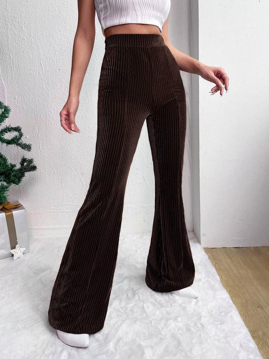 Person wearing brown ribbed flared pants and a white top on a light background