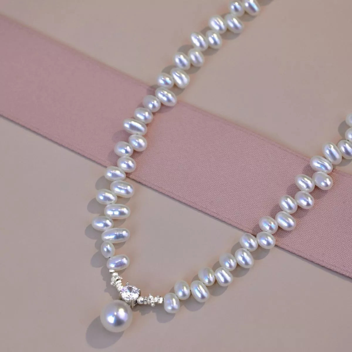 Pearl necklace with a diamond clasp on a pink and beige background
