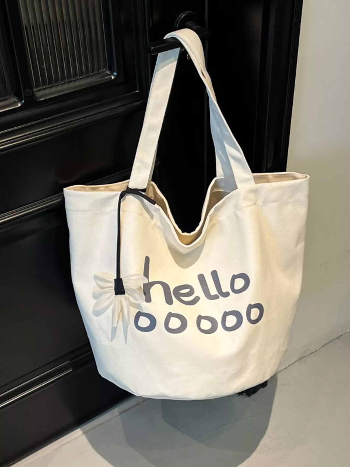 White tote bag with 'hellooooo' text on a black surface