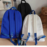 Two backpacks, one blue and one white, with blue straps on a wooden surface.