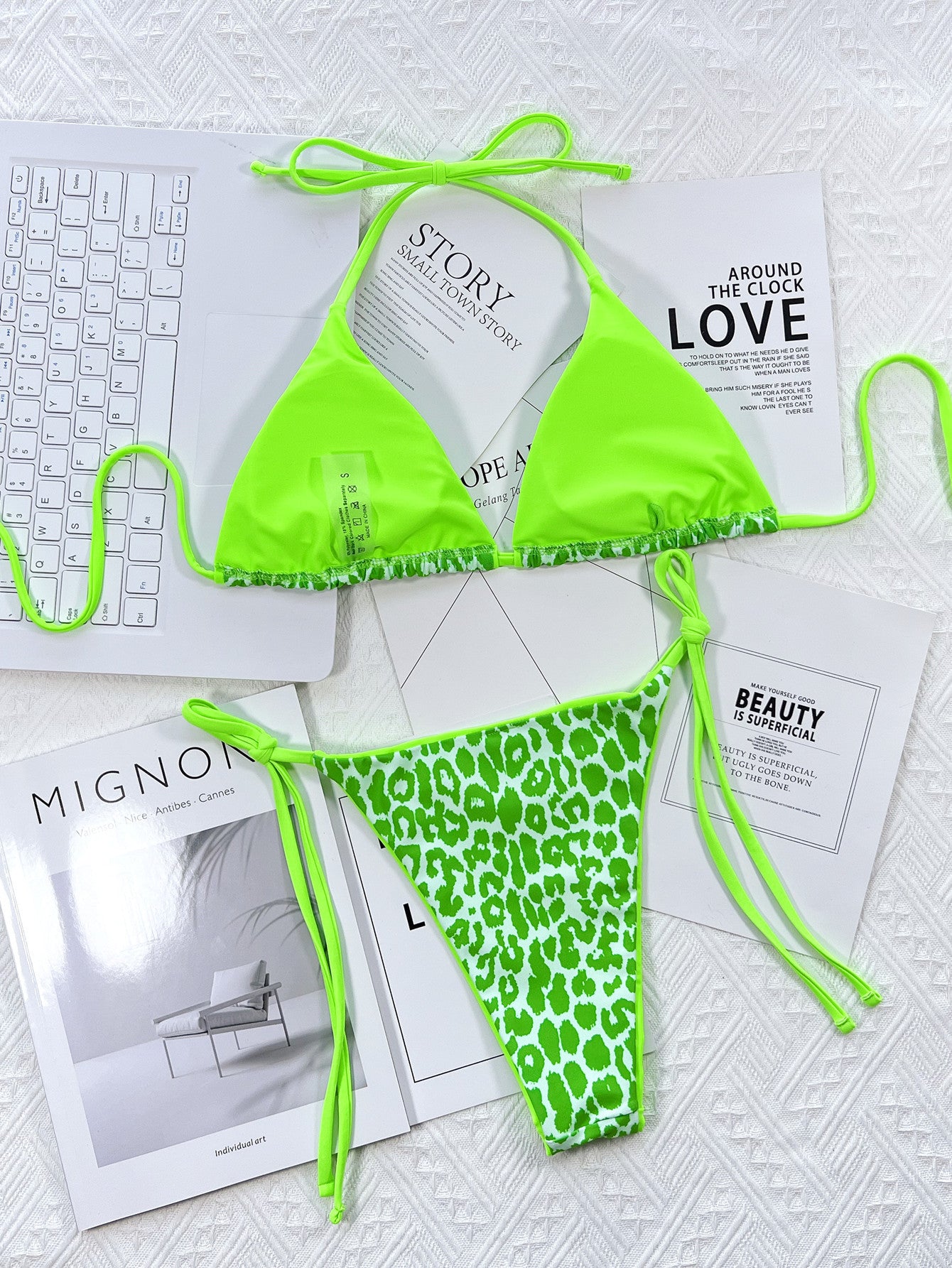 Neon green bikini set on a textured surface with magazines underneath