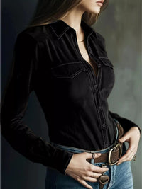 Woman wearing a black long-sleeve shirt and blue jeans against a dark background