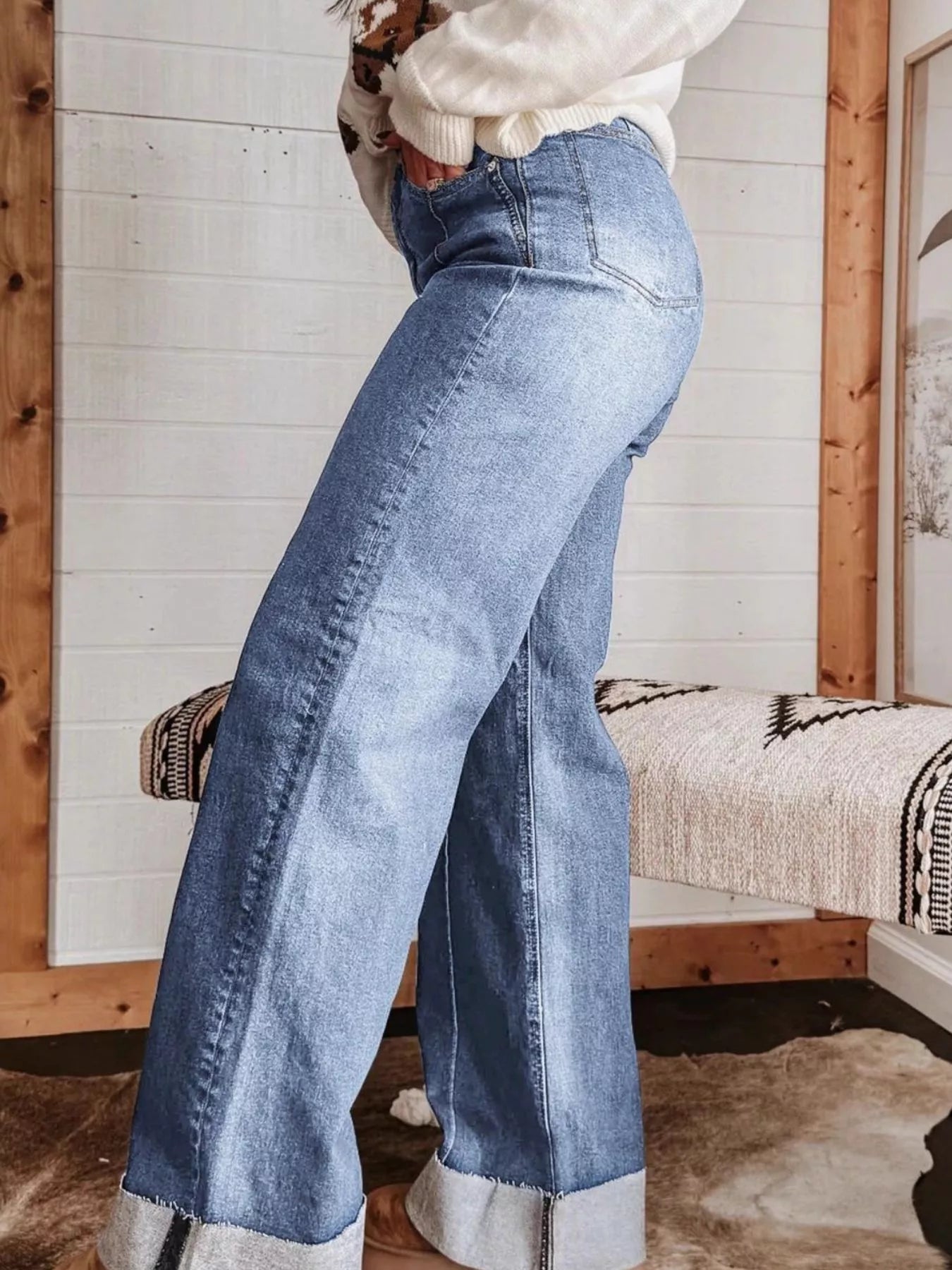 Person wearing blue flared jeans in a room with wooden walls and a bench.