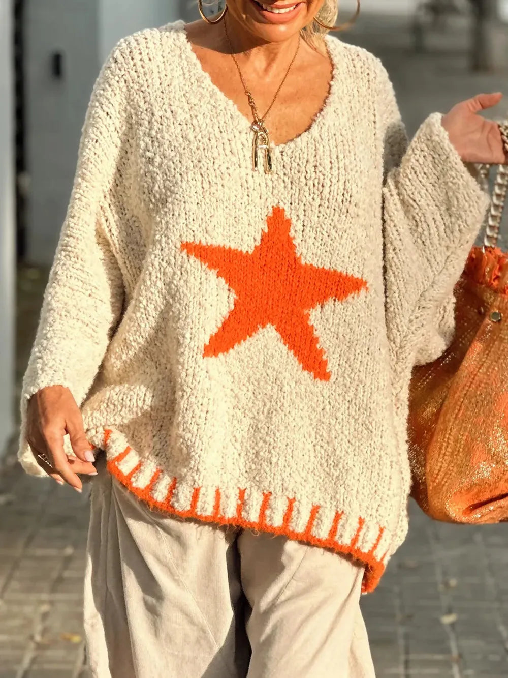 Person wearing a beige sweater with an orange star design outdoors.