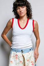 Woman wearing a white tank top with red trim and floral pants against a plain background