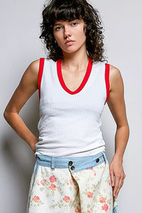 Woman wearing a white tank top with red trim and floral pants against a plain background