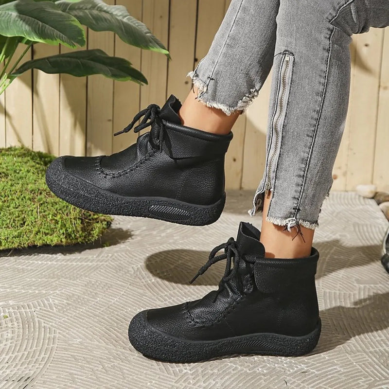Person wearing black boots with a wooden fence and greenery in the background