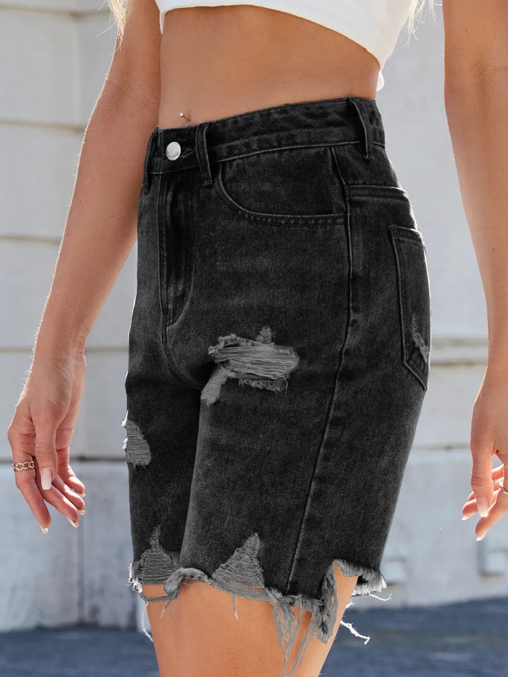 Black denim shorts with distressed details worn by a person.