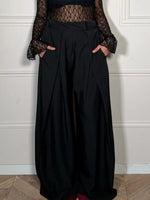 Person wearing a black outfit with a sheer top against a white wall.