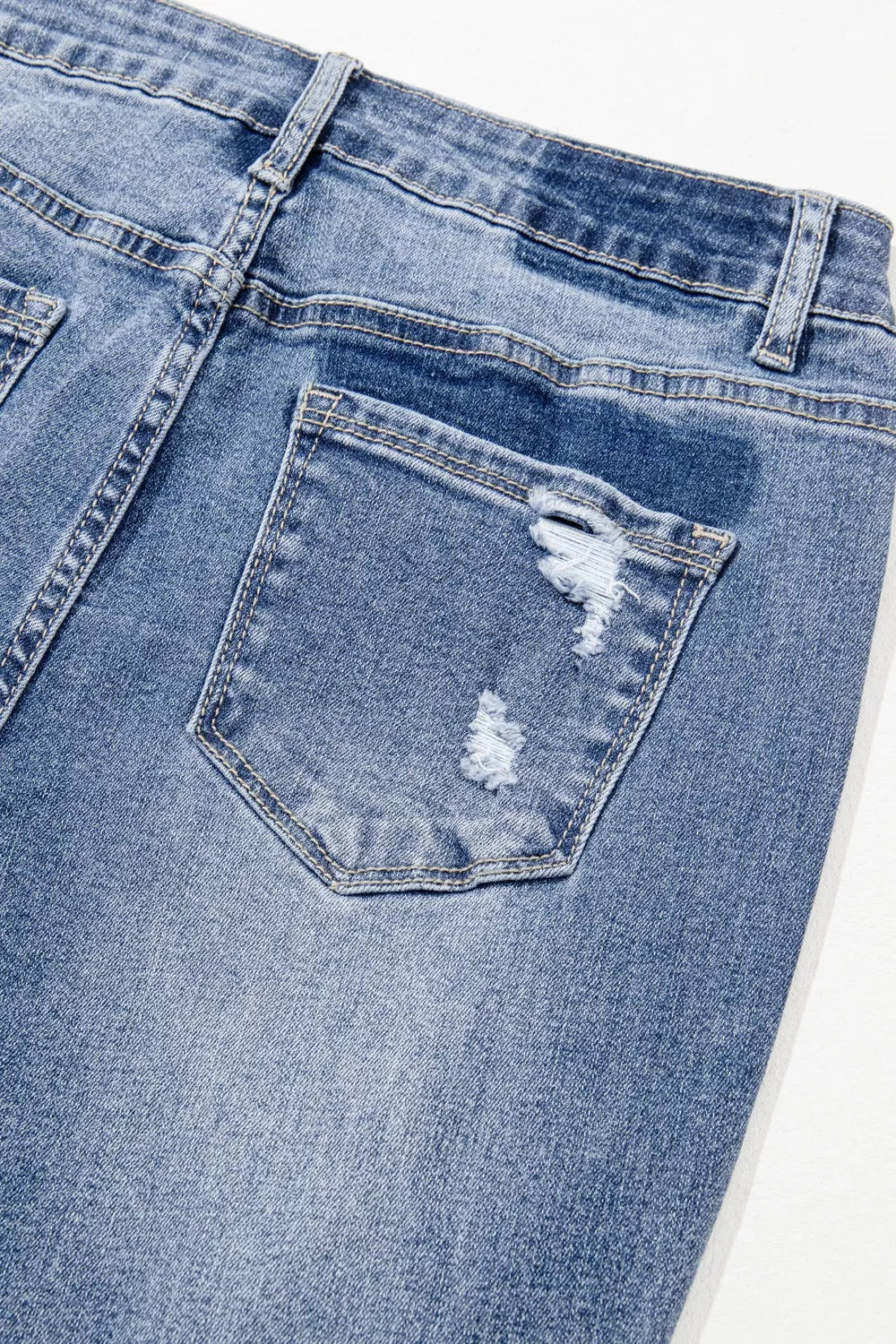 Close-up of blue jeans with a pocket showing distressing details on a white background