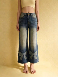 Person wearing blue jeans with bow designs on a beige background