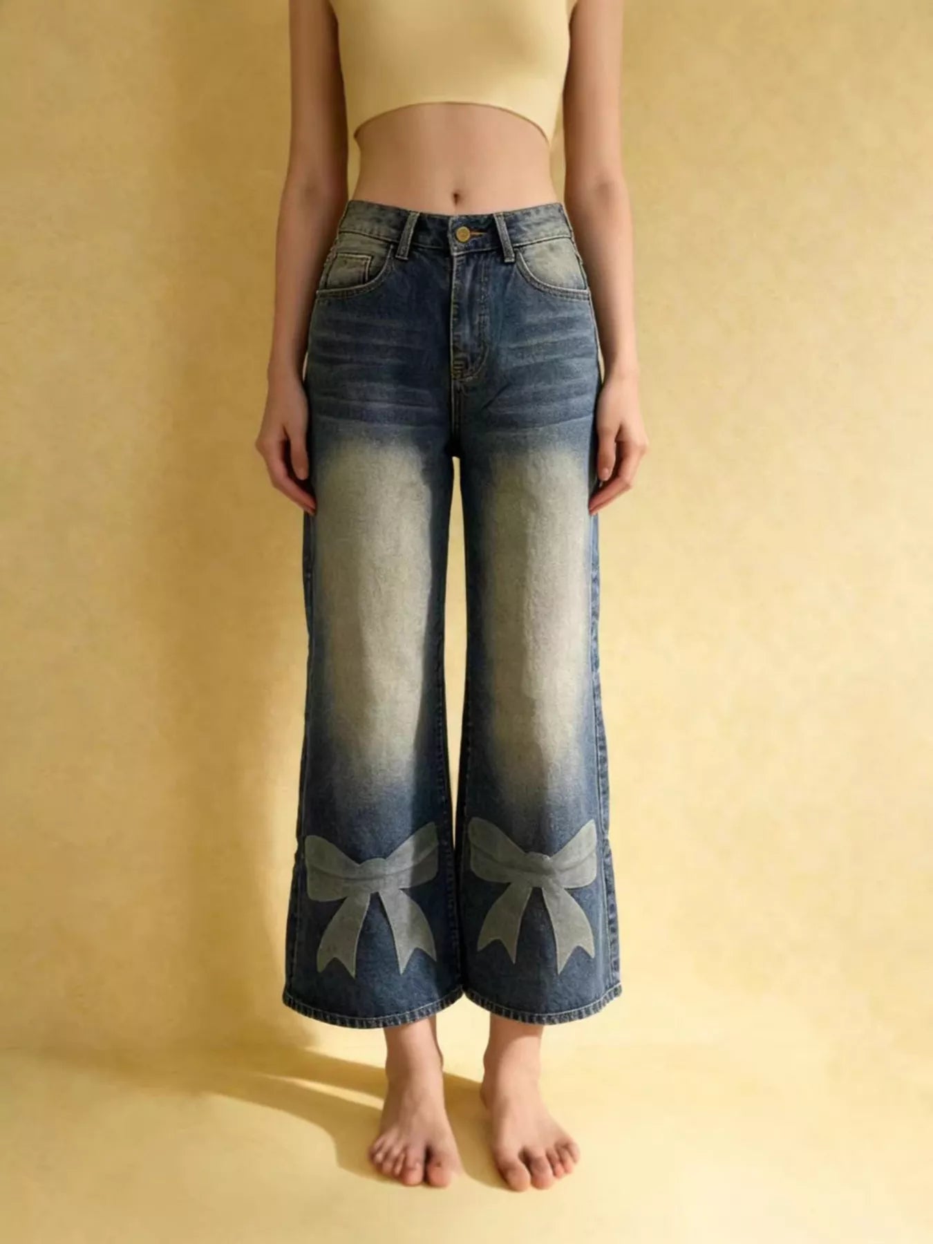 Person wearing blue jeans with bow designs on a beige background