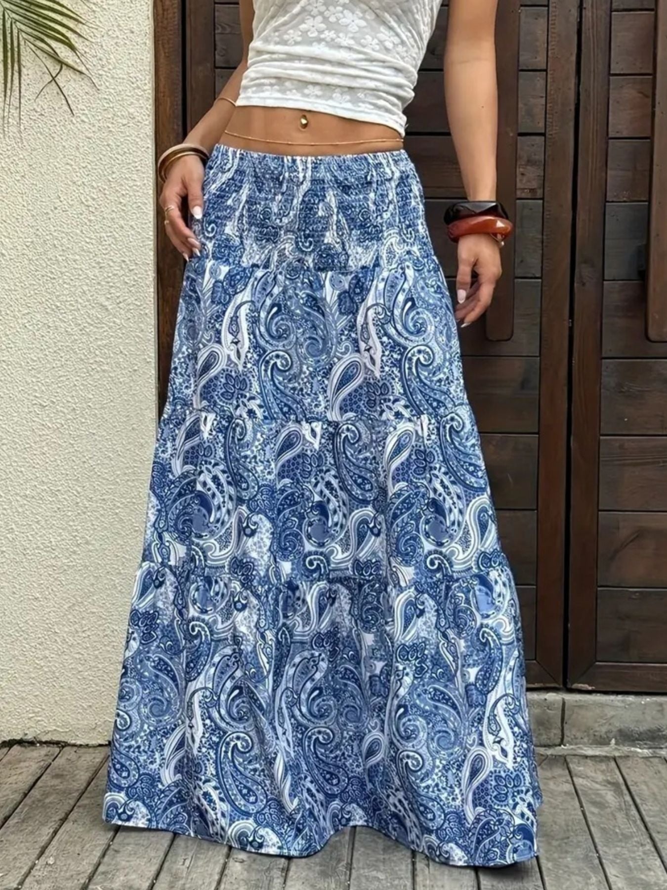 Person wearing a blue paisley patterned skirt standing against a wooden door.