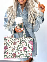 Person holding a floral-patterned tote bag and a Starbucks cup against a white background