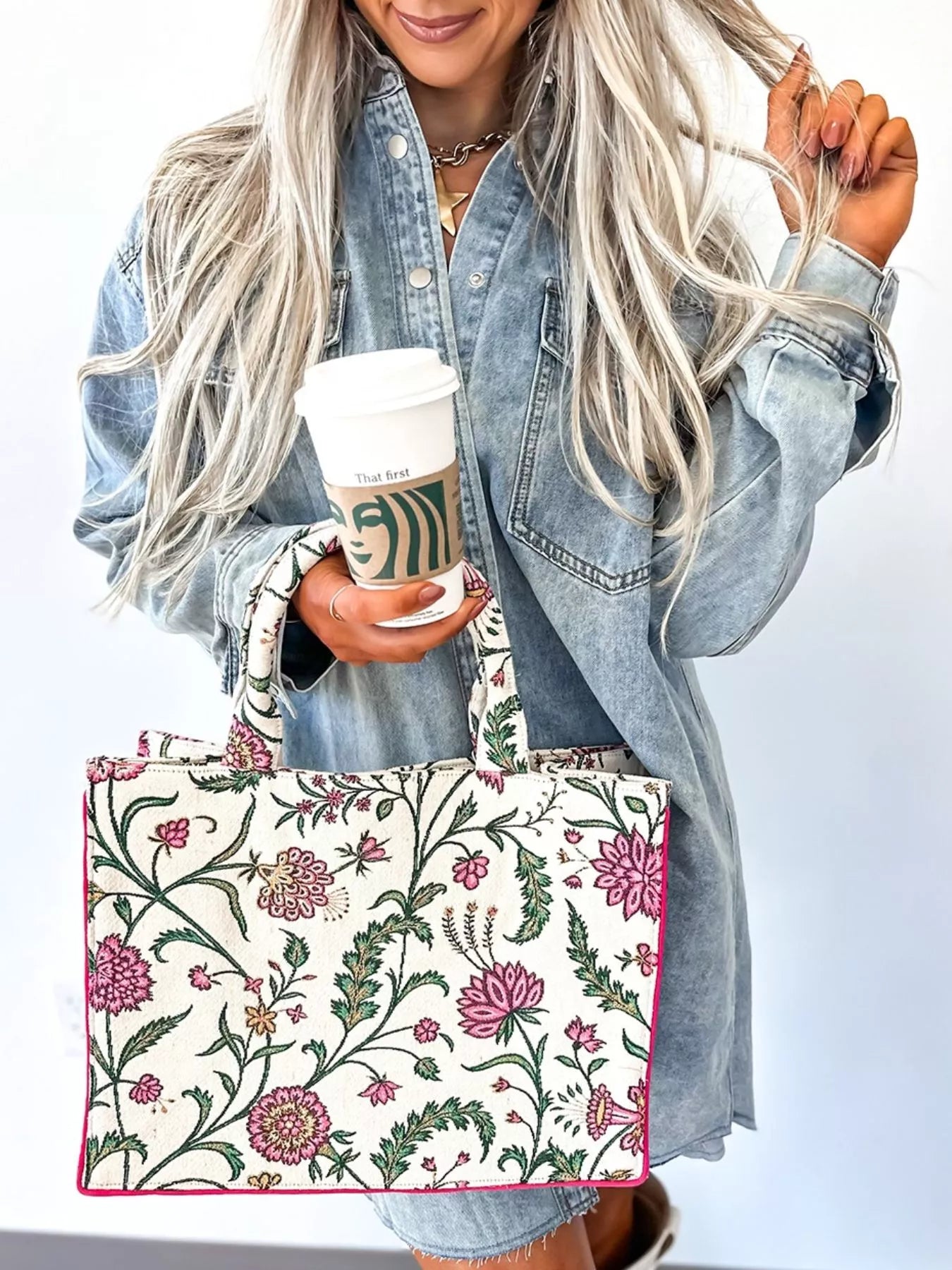 Person holding a floral-patterned tote bag and a Starbucks cup against a white background