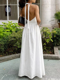 Woman in a white dress standing outdoors with greenery and a building in the background