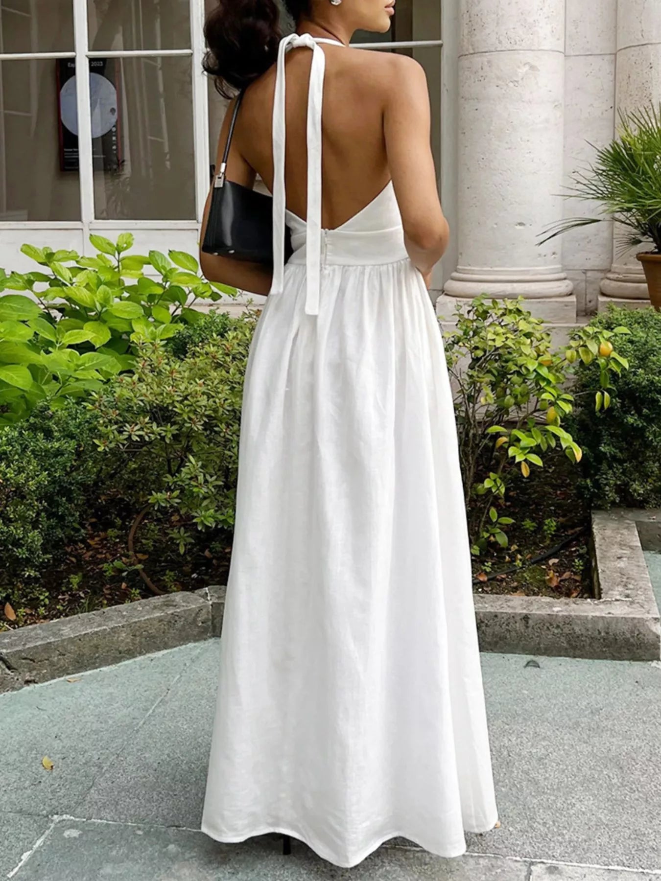 Woman in a white dress standing outdoors with greenery and a building in the background