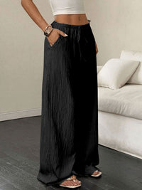 Person wearing black wide-leg pants in a minimalistic room with a white sofa.