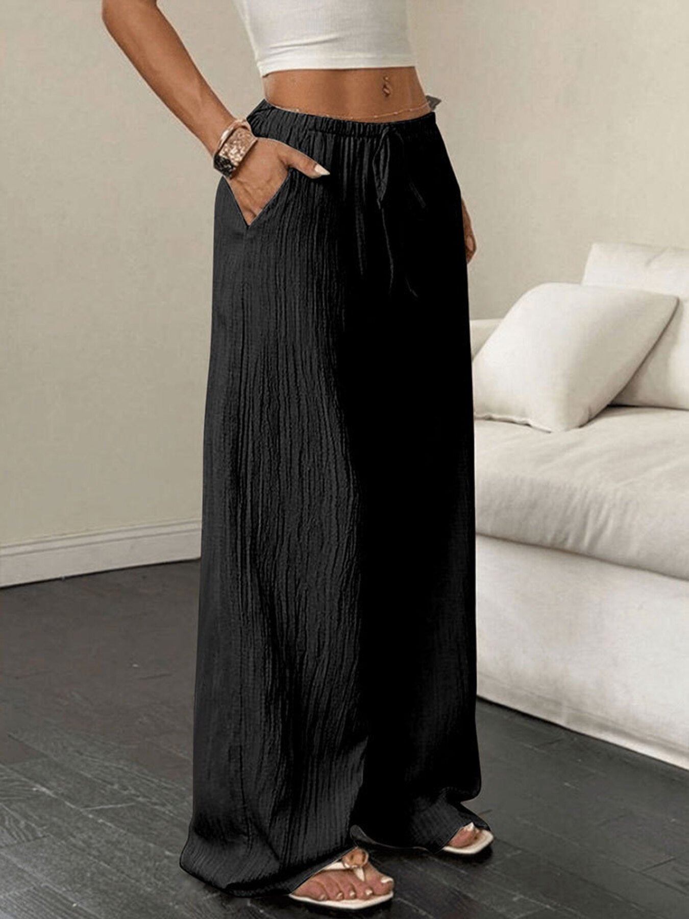 Person wearing black wide-leg pants in a minimalistic room with a white sofa.