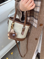 Person holding a beige handbag with a brown strap, wearing a plaid scarf and coat.