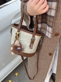 Person holding a beige handbag with a brown strap, wearing a plaid scarf and coat.