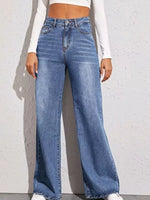 Person wearing blue wide-leg jeans against a white brick wall.
